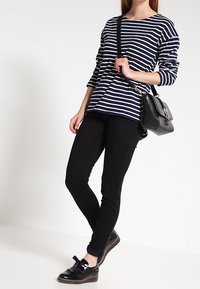 Marinblå och vitrandig långärmad tröja, svarta skinny jeans och svarta skor med en rosett. Liten svart handväska med axelrem.