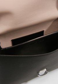 Sac à main en cuir noir avec intérieur beige, doté d'un fermoir argenté et du nom de la marque embossé à l'intérieur.