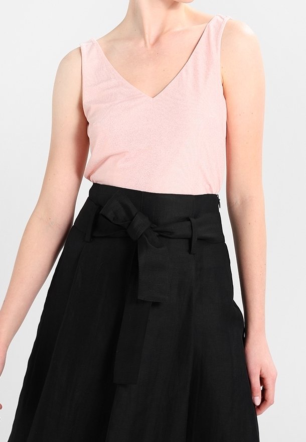 Jasnoróżowy top bez rękawów z dekoltem w serek, zestawiony z czarną spódnicą o wysokim stanie z dużą kokardą w talii i swobodną sylwetką.