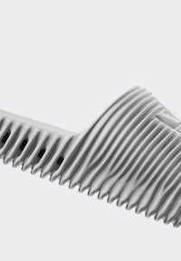 Elastisk slidesandal i ljusgrått, med en vågig ribbad textur, öppen design och ventilationshål längs sulan för andningsförmåga.