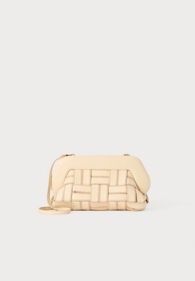 Sac à main tissé beige avec un design structuré, présentant un dessus lisse et une longue bandoulière. Des détails texturés rehaussent l'apparence générale.