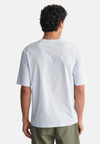Camiseta de algodón azul claro con cuello redondo y mangas cortas, que presenta una textura suave y un ajuste holgado. Solo vista posterior.