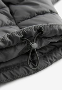 Gecodan negru de tip puffer, în prim-plan, având o textură matlasată, închidere cu șnur elastic și material neted, lucios.