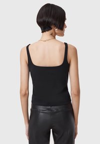 Fekete, rövidített tank top négyzet alakú dekoltázzsal és keskeny pántokkal, sima, feszes textúrával. A modell bőrnadrággal viseli.