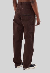 Pantaloni cargo marroni con una vestibilità rilassata, multiple tasche, accessori in metallo argentato e dettaglio a contrasto in vita. Tessuto texture con una finitura pulita.