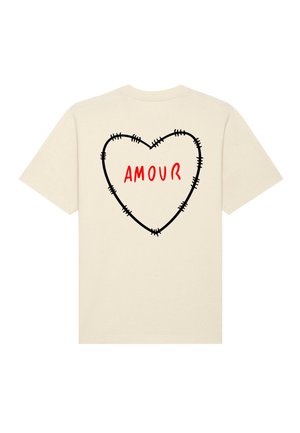 T-shirt crème avec un motif de cœur noir cousu et le mot "AMOUR" en rouge gras au centre. Manches courtes et encolure ronde.