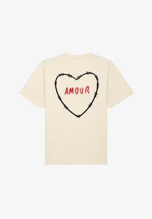 T-shirt crème avec un motif de cœur noir cousu et le mot "AMOUR" en rouge gras au centre. Manches courtes et encolure ronde.