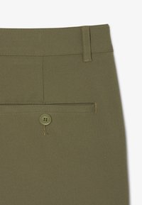 Pantalones verde oliva con una textura suave, que cuentan con un bolsillo trasero y un botón con detalle de logo grabado. Costuras en un color contrastante.