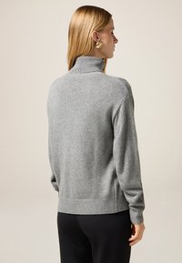 Maglione grigio a collo alto con orlo e polsini a coste, realizzato in morbido tessuto a maglia. Texture liscia, vestibilità ampia e design minimalista.