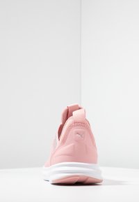 Sneaker atletica rosa con suola bianca vista da dietro, dotata di tallone per il piede e logo Puma sul tallone, posizionata su sfondo bianco uniforme.