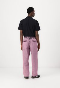 Svart kortermet polo-skjorte kombinert med løstsittende, rosa denim bukser med teksturert overflate og elastisk liv. Svart sneakers med striper.