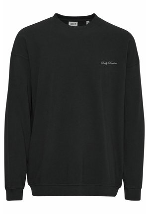 Mustasta puuvillapuserosta, jossa on pyöreä kaula-aukko, pitkät hihat, resorit hihoissa ja hillitty brodeerattu teksti "Päivittäinen Rutiini" rinnassa.