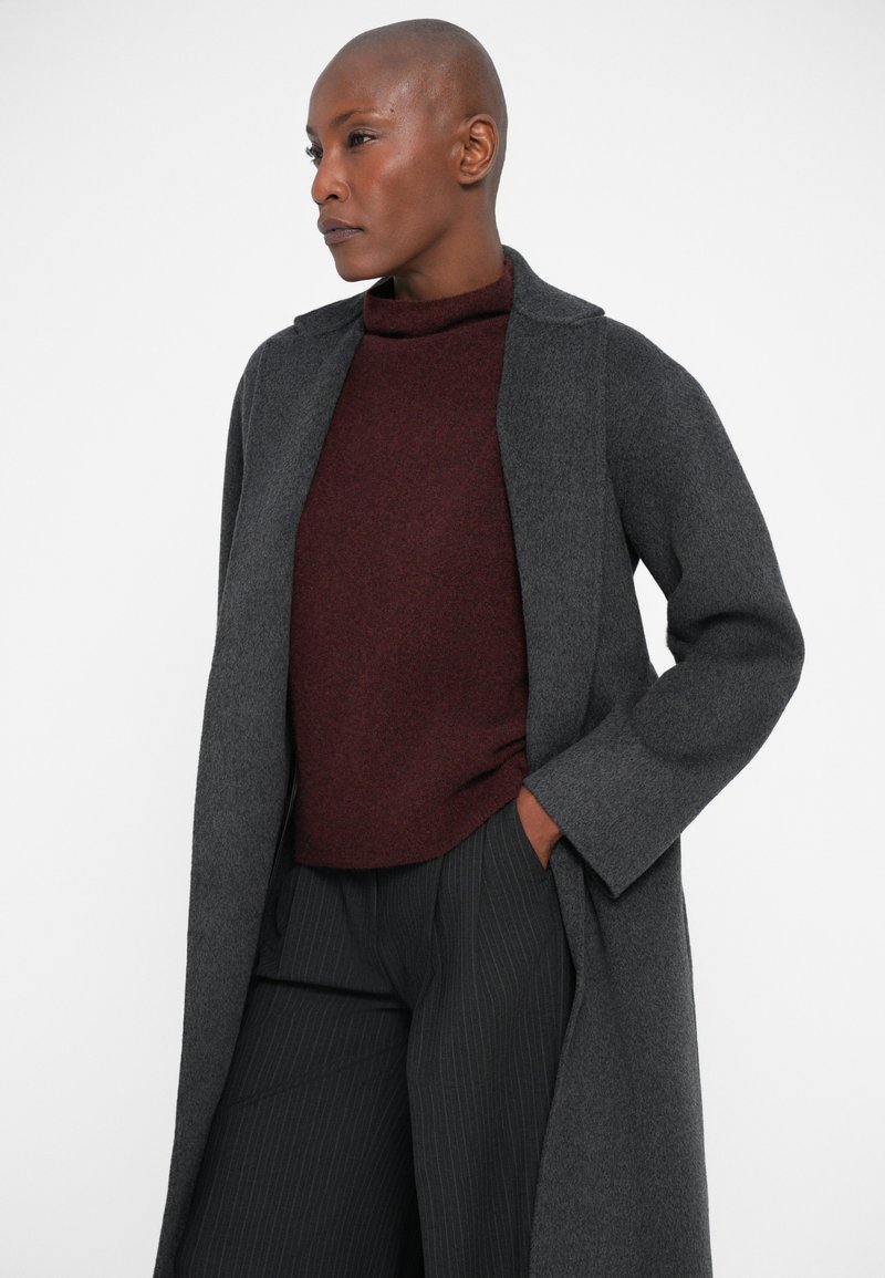 Grey wool coat with a notched collar, worn over a burgundy turtleneck sweater and pinstriped trousers. Smooth texture, long sleeves.