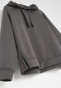 Szara bluza z kapturem o luźnym kroju, z sznurkiem do regulacji, rękawami raglanowymi i bocznymi rozcięciami przy hemie dla zwiększonej swobody ruchów.