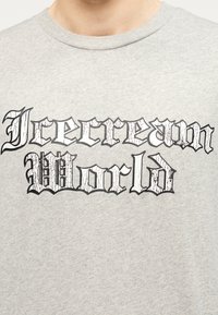 Γκρι βαμβακερό t-shirt με έντονα μαύρα ραγισμένα γράμματα που γράφουν «Icecream World». Σχεδίαση με κανονικό λαιμό και απαλή υφή.