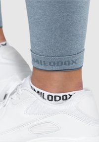 Jasnoniebieskie legginsy z mankietem i subtelnym logo. Połączone z białymi butami sportowymi i czarno-białymi skarpetkami do kostek.