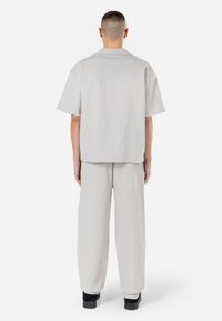 Camisa cinza de manga curta com um acabamento ligeiramente texturizado, combinada com calças largas igualmente cinzas, ambas feitas de material leve. Sapatos pretos.