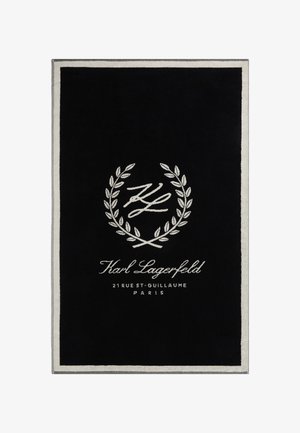 Black rectangular rug with a plush texture, featuring a white embroidered logo and laurel design, bordered with a light gray trim.