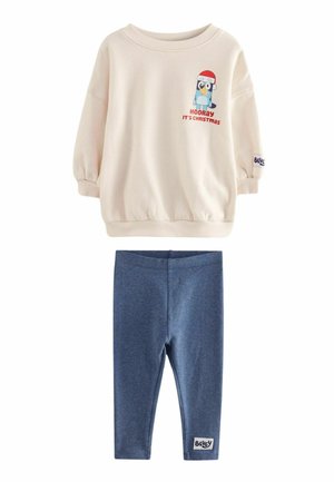 Ljuscremefärgad sweatshirt med en tecknad pingvin-grafik och röd text, parat med mörkblå leggings med en varumärkesskylt på midjebandet.
