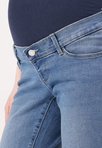 Maternity jeans in medium blue denim, featuring a smooth waistband, front pockets, and a classic button closure with subtle fading details.