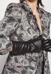 Blazer su misura con motivo paisley ornato in tonalità di nero e azzurro chiaro; presenta spalle strutturate, colletto a revers e tasca frontale. Guanti in pelle nera.