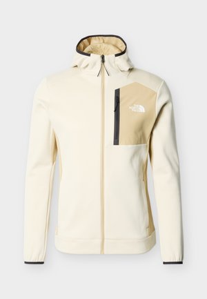 Chaqueta con capucha de color beige claro con cremallera, bolsillo en el pecho de color beige más oscuro y cremallera negra, con el logotipo de The North Face en el bolsillo.