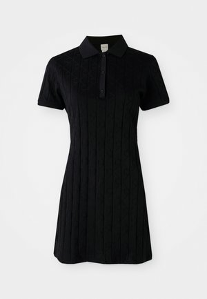 Robe polo noire à manches courtes, avec un col et un motif texturé de diamants et de cercles. Fermeture à boutons au niveau du cou.
