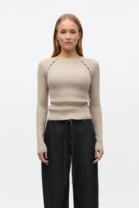 Bēša ribveida adīta džemperis ar garām piedurknēm un dekoratīvām šuvēm uz pleciem, kombinēts ar tumšas džinsa augsta vidukļa biksēm ar auklu jostu.