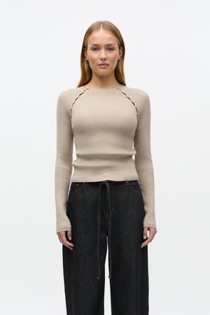 Beige ribstrikket striktrøje med lange ærmer og dekorative sømme ved skuldrene, kombineret med mørk denim højttaljede bukser med snøre.