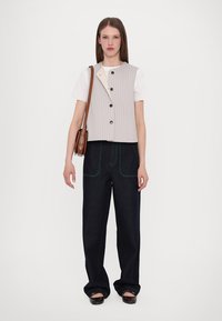 Gilet à rayures gris clair avec des boutons noirs sur un t-shirt blanc, associé à un pantalon en denim foncé avec des coutures et des poches vertes contrastantes.