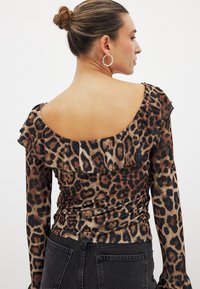 Leopard print top with long sleeves and a ruffled neckline. Made of smooth fabric, featuring a low back design and form-fitting silhouette.