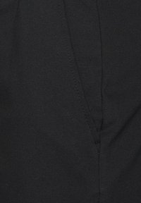 Tessuto nero con cucitura diagonale e dettagli di cucito, che mostrano parte di una tasca o di una sezione ripiegata su un indumento.