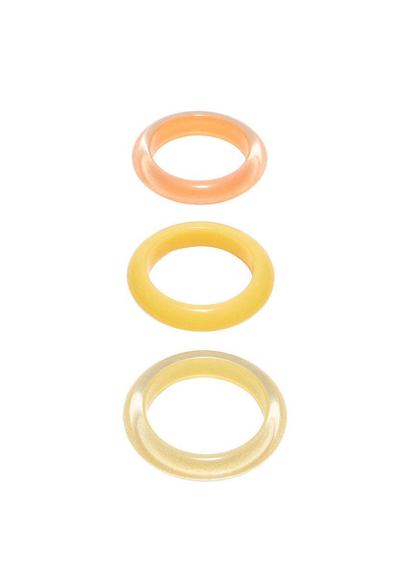 Trois anneaux translucides en silicone orange, jaune et jaune clair disposés verticalement sur un fond blanc.