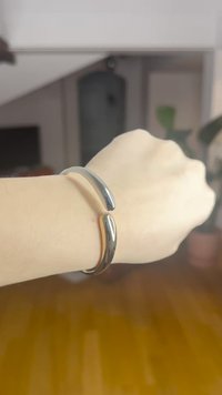 Metallist käevõru, millel on sile ja läikiv pind, kaardus disain, mis kattub avausel; hõbe- ja kullatoonid.