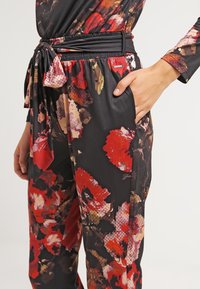 Pantaloni neri con motivo floreale, caratterizzati da fiori rossi e rosa, tessuto morbido, vita elastica con dettaglio a laccio e tasche laterali.