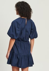 Tyrkysové šaty s puff-sleeve rukávmi a elastickým pásom. Obsahujú volánový lem a otvor na chrbte v tvare kľúča, vyrobené z ľahkého materiálu.