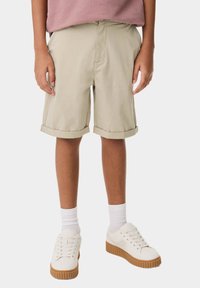 Beige knälånga shorts med upprullade muddar, gjorda av lättviktig tyg. Matchat med vita sneakers och ribbade vita strumpor.