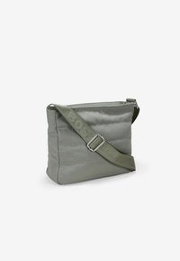 Bolso de hombro rectangular acolchado en verde suave, fabricado con tela lisa. Presenta una correa texturizada con detalle de logo y una hebilla plateada.