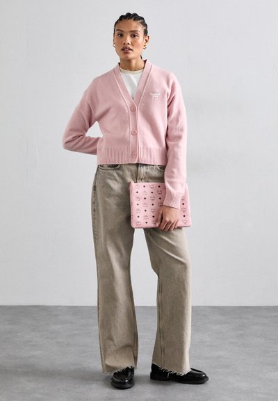 Lichtroze gebreide cardigan met een sjalkraag en drie knopen, gecombineerd met losse beige broeken en een gestreepte rozenkleurige clutch.