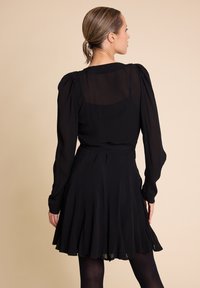 Svart kjole med lange, puffete ermer, en tettsittende liv og en utsvingt skjørt. Laget av lett stoff med en gjennomsiktig bakpanel.