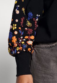 Μαύρη φούτερ μπλούζα με πολύχρωμα λουλουδάτα κεντήματα σε πορτοκαλί, κίτρινο, ροζ, μωβ και μπλε, με ριμπ μανσέτες και άνετη εφαρμογή.