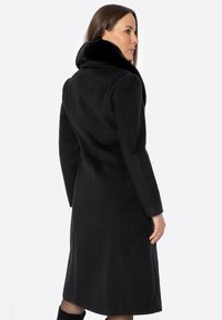 Czarny wełniany płaszcz z miękkim kołnierzem, dopasowanym krojem, długimi rękawami i długością do kolan o gładkiej fakturze.