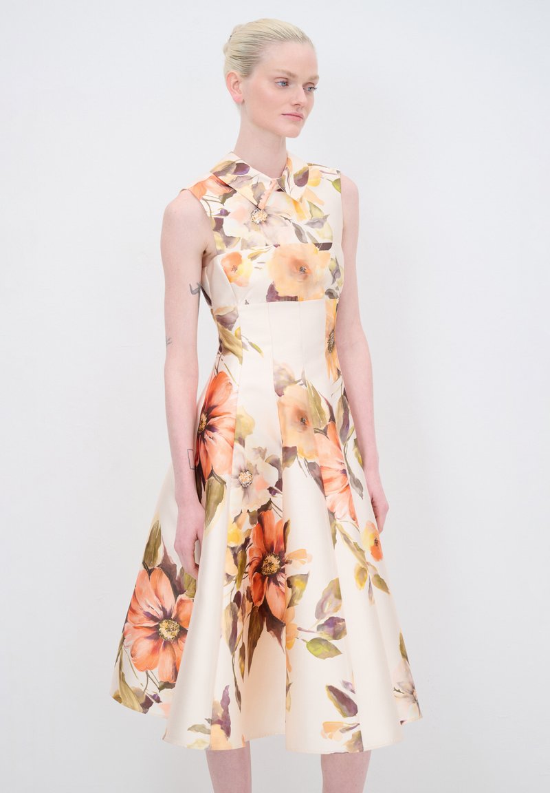 Blumenkleid mit tailliertem Oberteil und ausgestelltem Rock, verziert mit orangefarbenen und gelben Blumenmustern auf einem cremefarbenen Hintergrund. Mit Kragen.