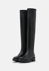 Svarta läderstövlar över knäet med en kraftig klack, rund tå och texturerad gummisula, med kontrasterande sömmar längs skaftet.