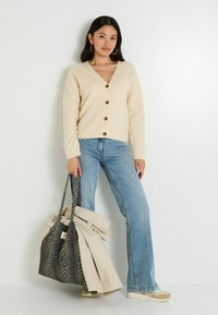 Cardigan beige en tricot avec un col en V, orné de boutons en bois, porté avec un jean flare bleu clair et un sac fourre-tout à imprimé léopard.