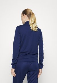 Marineblaue Sportjacke mit hohem Kragen, langen Ärmeln und taillierter Passform, ausgestattet mit einer weichen, glatten Textur.