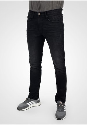 Svarta jeans i denim med figursydd design, lätt slitna detaljer och klassisk femficksstil. Bärs med grå sneakers och en grå T-shirt.