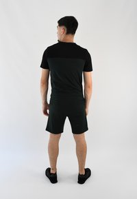 Ropa deportiva negra y verde oscuro: camiseta ajustada de manga corta con una franja horizontal negra, emparejada con pantalones cortos a juego, llevada con zapatos negros.