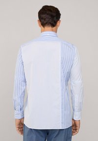 Camicia a maniche lunghe con righe verticali blu e bianche, caratterizzata da un colletto a bottoni e accenti sui polsini. Tessuto morbido con una texture liscia.