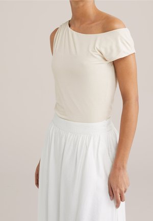 Jasno beżowa bluzka typu off-the-shoulder z krótkimi rękawami, wykonana z gładkiego materiału, w połączeniu z białą, zwiewną spódnicą do kostek z elastycznym pasem.